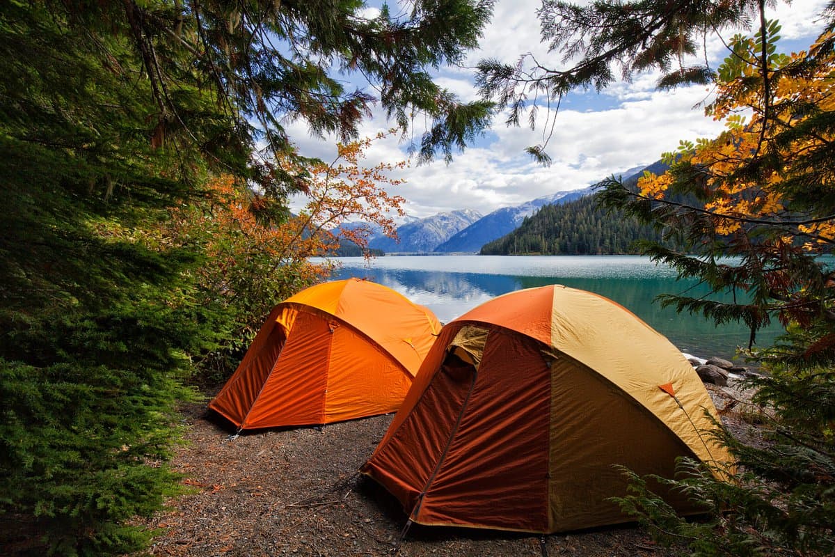 Camping tents beside a Himalayan lake surrounded by forest and mountains